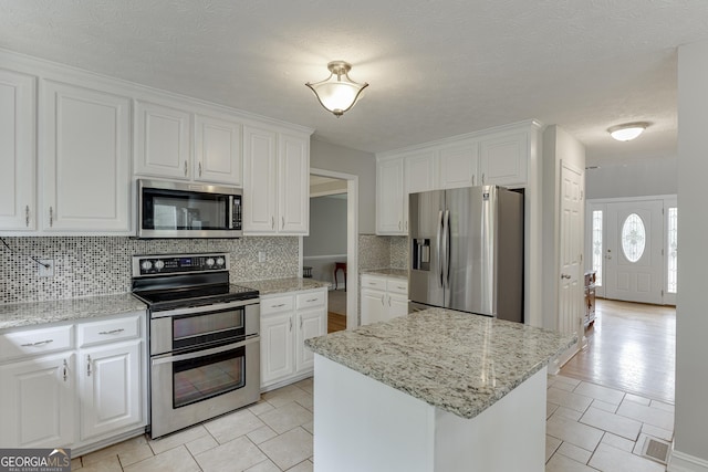 5922 Terrace Lake Pt, Flowery Branch, GA 30542 - kitchen with appliances with stainless steel finishes, decorative backsplash, white cabinetry, light stone counters, and light tile patterned flooring
