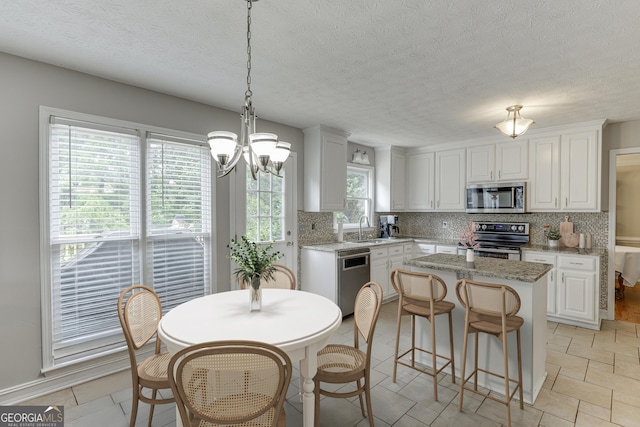5922 Terrace Lake Pt, Flowery Branch, GA 30542 - kitchen with appliances with stainless steel finishes, a center island, backsplash, a chandelier, and white cabinets