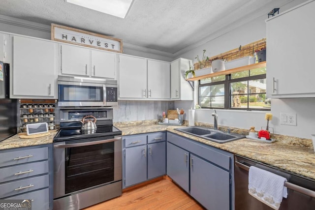 kitchen featuring appliances with stainless steel finishes, a sink, light wood-style floors, a textured ceiling, and white cabinetry