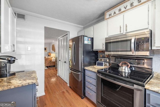 kitchen with visible vents, ornamental molding, white cabinets, light wood finished floors, and appliances with stainless steel finishes