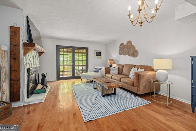 living room with a textured ceiling, a stone fireplace, wood finished floors, baseboards, and a notable chandelier