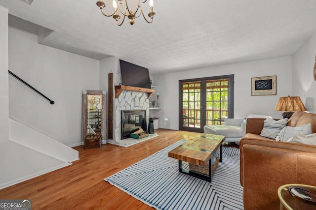 living area featuring a chandelier, a stone fireplace, baseboards, wood finished floors, and stairway
