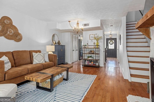 living room with a textured ceiling, visible vents, a notable chandelier, stairs, and hardwood / wood-style floors