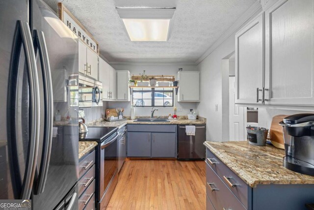 kitchen featuring a textured ceiling, light wood-type flooring, a sink, white cabinets, and stainless steel appliances