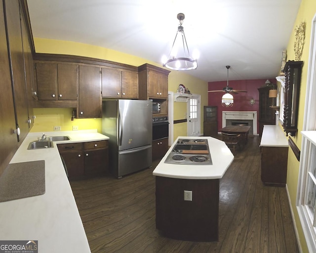 kitchen featuring a kitchen island, appliances with stainless steel finishes, a fireplace, a sink, and dark wood-type flooring