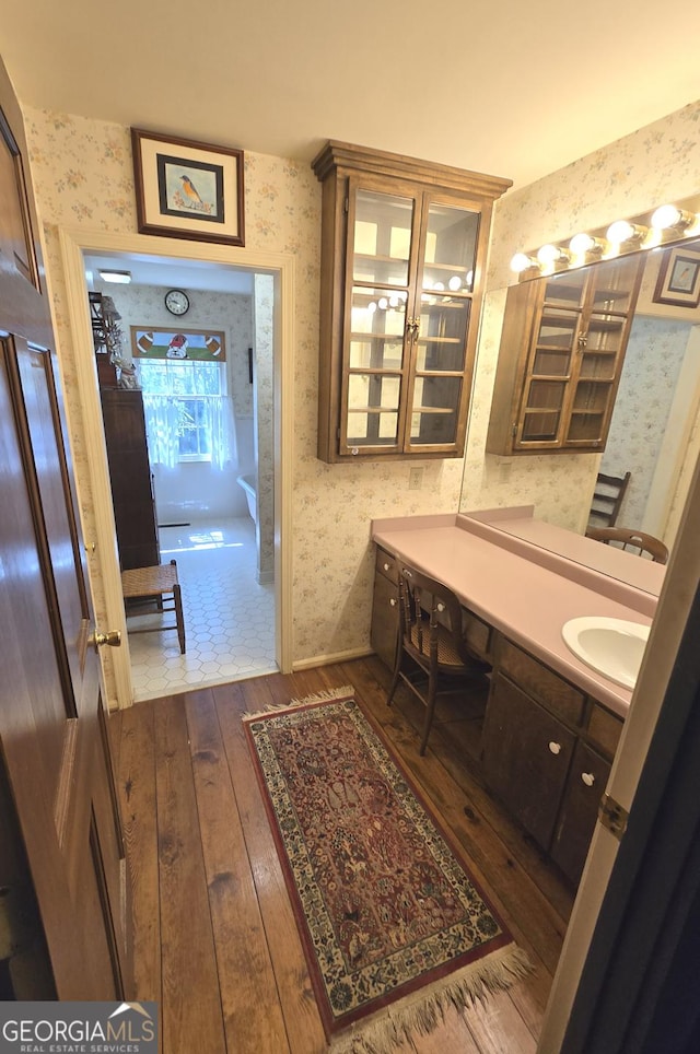 bathroom with wood-type flooring, baseboards, vanity, and wallpapered walls