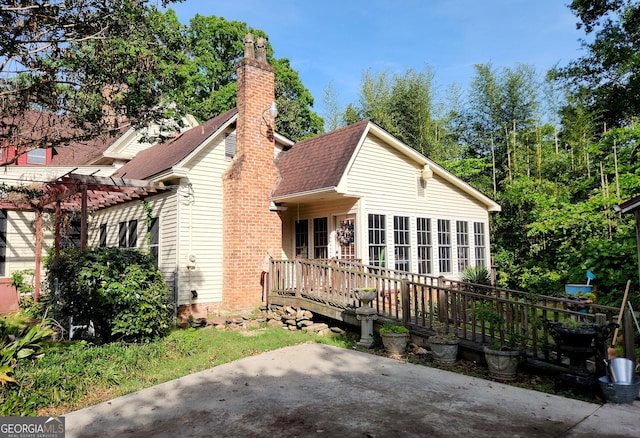 view of front facade with a patio, a shingled roof, a chimney, and a deck