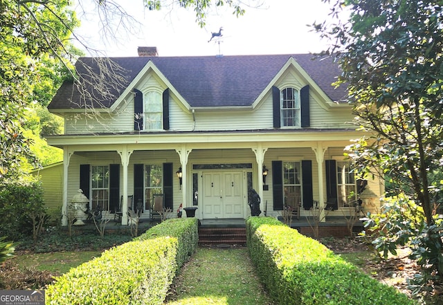 view of front of house featuring a porch, a chimney, and a shingled roof
