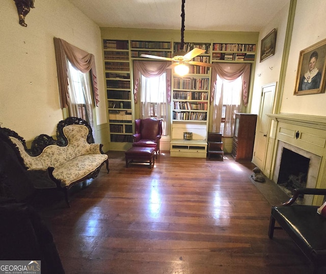 living area with built in shelves, ceiling fan, a fireplace, and wood finished floors