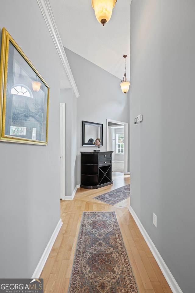 hall with baseboards, light wood-style floors, and high vaulted ceiling