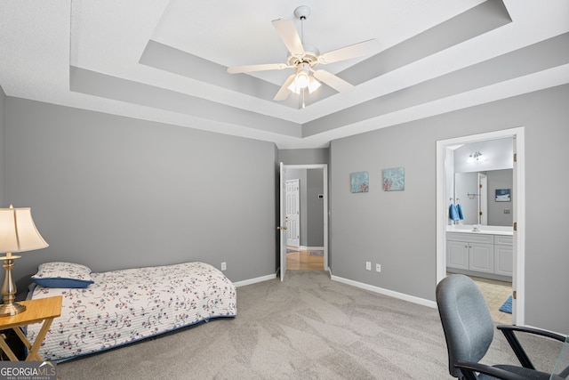 bedroom featuring a tray ceiling, light carpet, baseboards, and ensuite bath