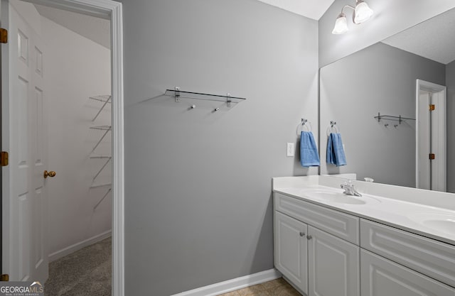 full bathroom with double vanity, baseboards, a sink, and a walk in closet