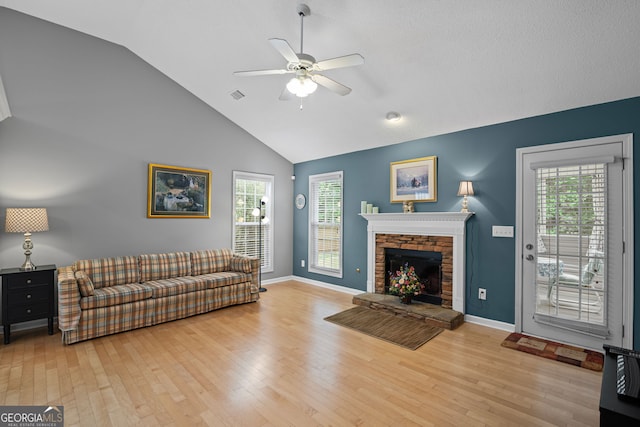 living room featuring a healthy amount of sunlight, ceiling fan, a stone fireplace, and wood finished floors