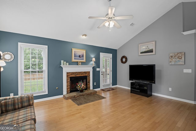 living room with baseboards, ceiling fan, a stone fireplace, and wood finished floors