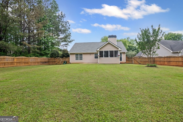 back of house with a lawn, a fenced backyard, a sunroom, and a chimney