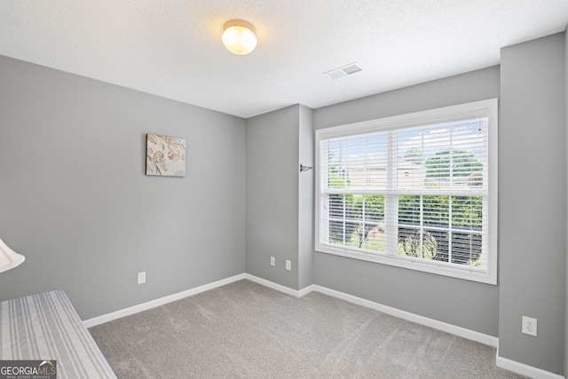 carpeted spare room featuring baseboards, a textured ceiling, and visible vents