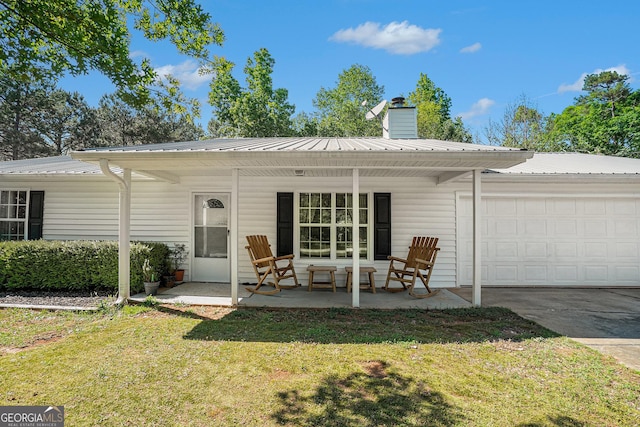 view of front facade featuring an attached garage, a front lawn, metal roof, a chimney, and driveway