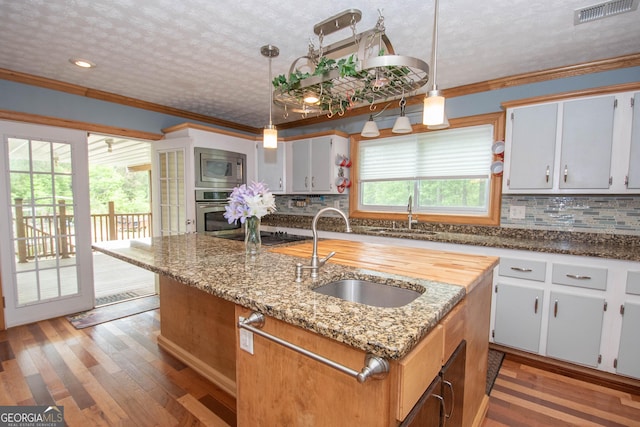 kitchen featuring visible vents, a sink, ornamental molding, stainless steel appliances, and an island with sink