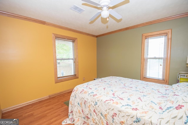 bedroom with visible vents, ornamental molding, wood finished floors, baseboards, and a ceiling fan
