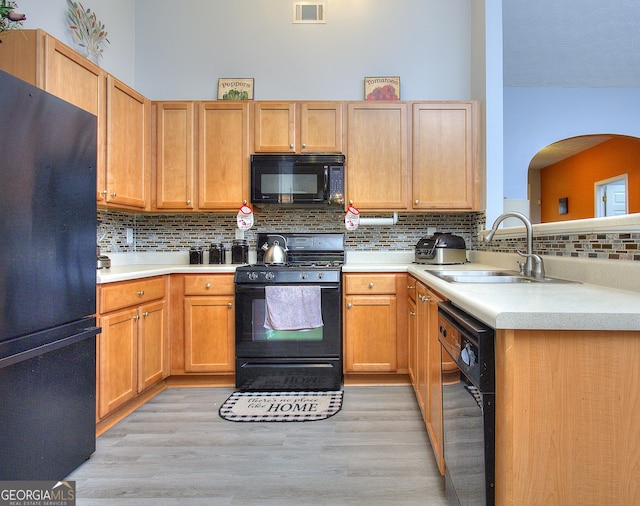 kitchen with visible vents, tasteful backsplash, light wood-type flooring, a sink, and black appliances