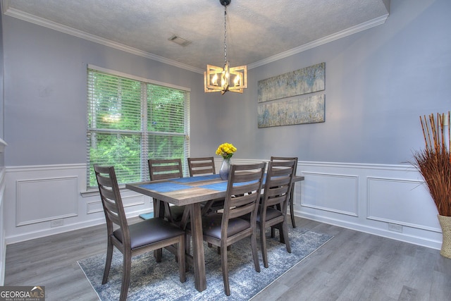 dining room featuring crown molding, wainscoting, wood finished floors, a notable chandelier, and a decorative wall