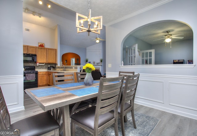 dining room featuring arched walkways, ceiling fan with notable chandelier, light wood-type flooring, and visible vents
