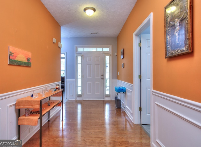 entrance foyer with wood finished floors, a textured ceiling, a decorative wall, and wainscoting