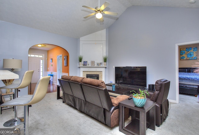 living area featuring a ceiling fan, a glass covered fireplace, lofted ceiling, carpet flooring, and arched walkways
