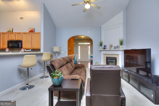 carpeted living area with visible vents, baseboards, ceiling fan, arched walkways, and vaulted ceiling