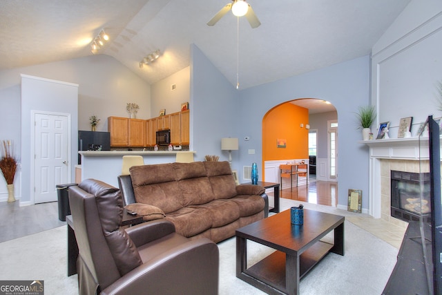 living room with arched walkways, rail lighting, a tiled fireplace, a ceiling fan, and visible vents