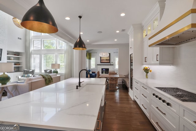kitchen with open floor plan, premium range hood, dark wood-type flooring, a large island with sink, and a sink