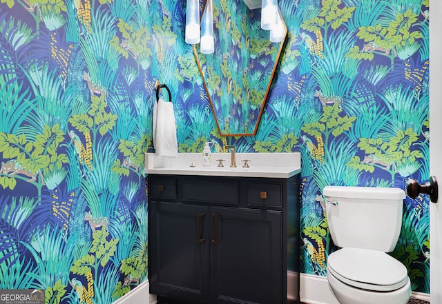 half bath featuring vanity, baseboards, toilet, and wallpapered walls