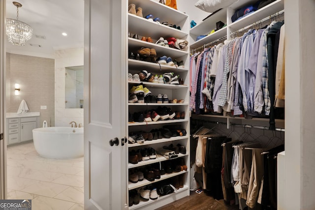 walk in closet with an inviting chandelier and marble finish floor