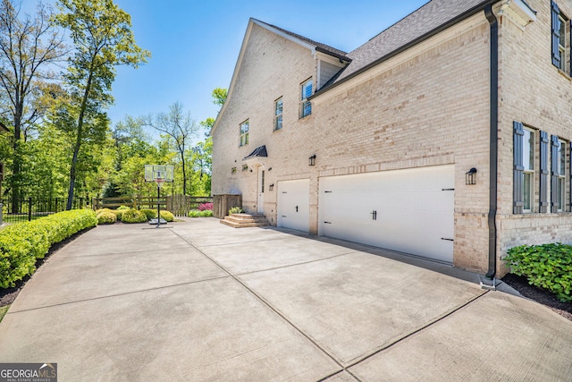view of home's exterior featuring brick siding, fence, and driveway