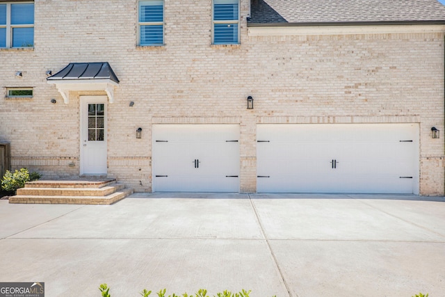 exterior space with a garage, a standing seam roof, brick siding, a shingled roof, and driveway
