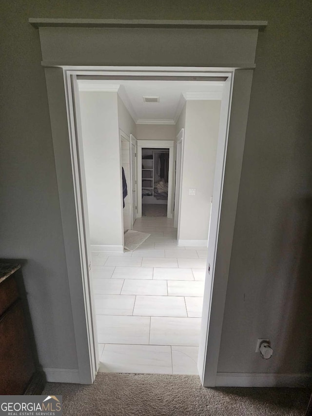 hall with light tile patterned floors, baseboards, ornamental molding, and visible vents