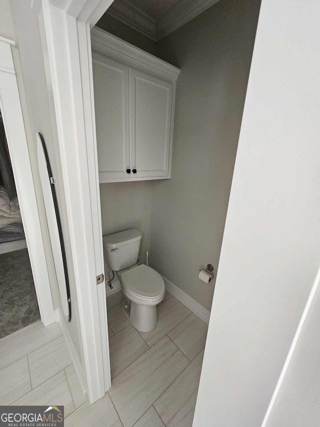 bathroom featuring baseboards, ornamental molding, and toilet