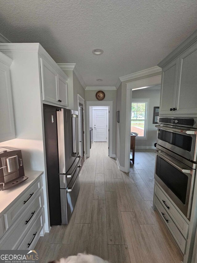 kitchen featuring ornamental molding, baseboards, white cabinetry, light wood finished floors, and stainless steel appliances