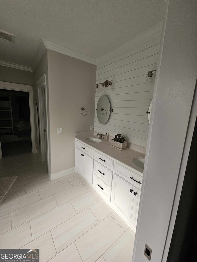 bathroom with double vanity, visible vents, crown molding, a sink, and baseboards