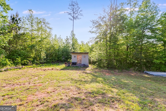 view of yard featuring a view of trees, an outdoor structure, and a storage unit