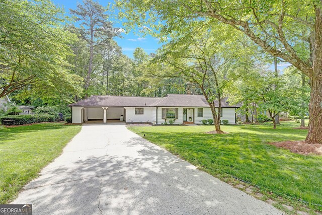 ranch-style home with concrete driveway, a front lawn, a carport, and view of scattered trees