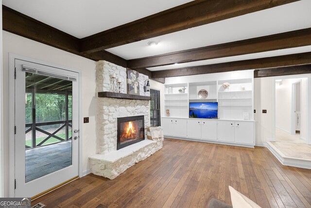 unfurnished living room featuring wood-type flooring, beam ceiling, a fireplace, and baseboards