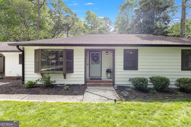 ranch-style house featuring a shingled roof and a front yard