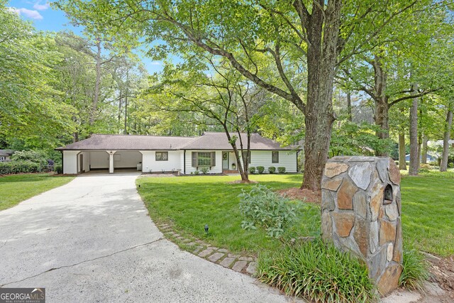 single story home featuring driveway, a front yard, an attached carport, and view of scattered trees