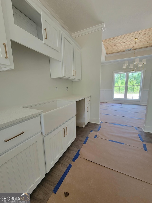 kitchen with crown molding, white cabinets, light stone countertops, a chandelier, and dark wood finished floors