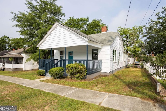 bungalow-style house featuring a shingled roof, a front lawn, covered porch, and a chimney