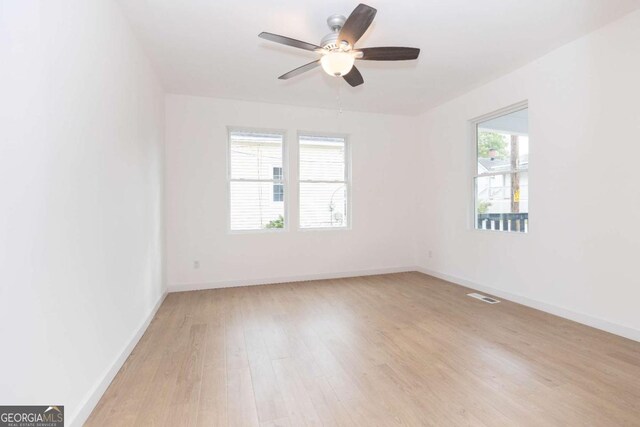 spare room with ceiling fan, visible vents, baseboards, and light wood finished floors