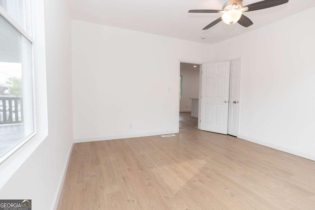 empty room with baseboards, a ceiling fan, light wood finished floors, and visible vents