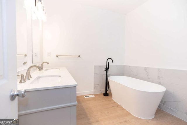 bathroom featuring visible vents, double vanity, wood finished floors, a freestanding bath, and a sink