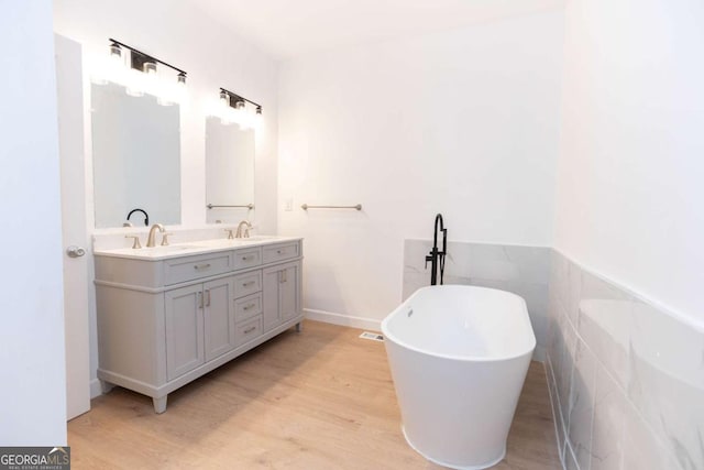 bathroom featuring a sink, a freestanding tub, double vanity, and wood finished floors